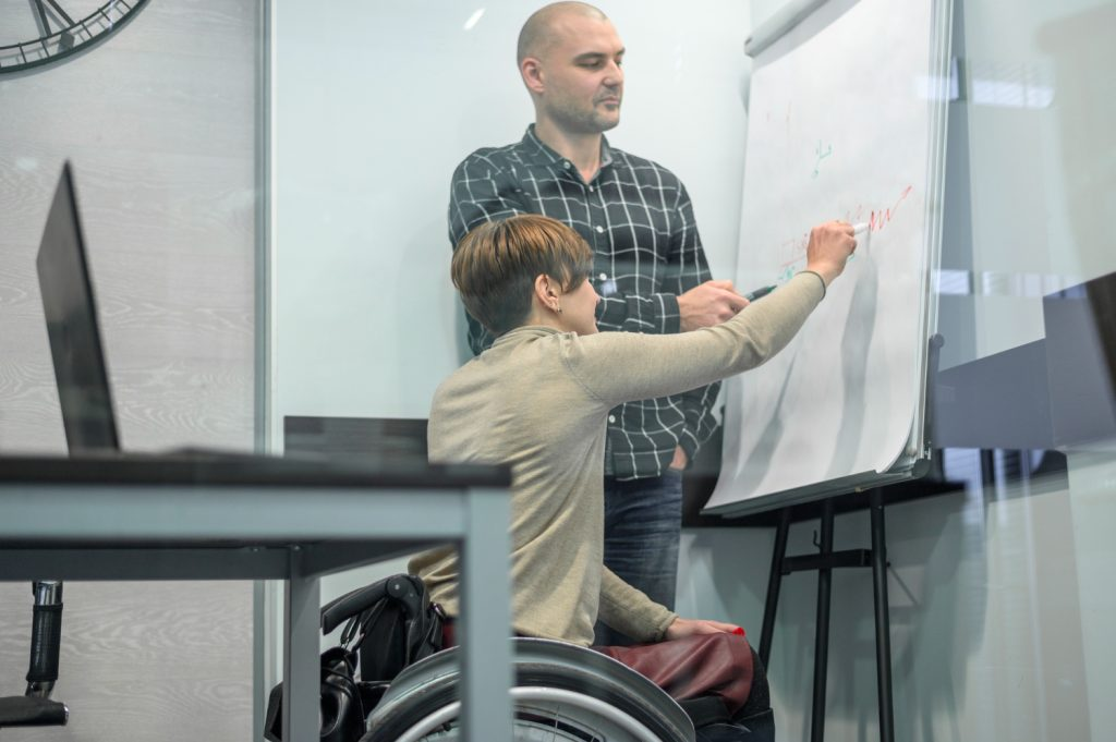 wheelchair user next to a bald man writing on a flipchart